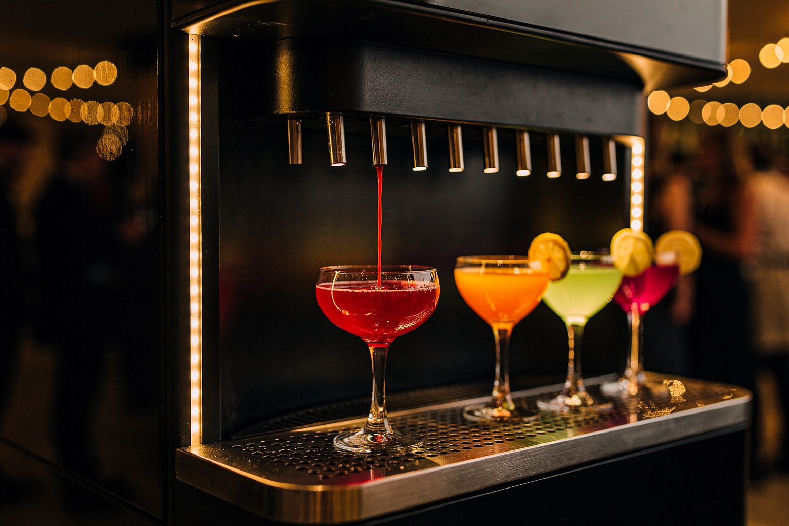 Illustration: an automated cocktail machine pouring a ruby-red drink into a coupe beside three finished cocktails