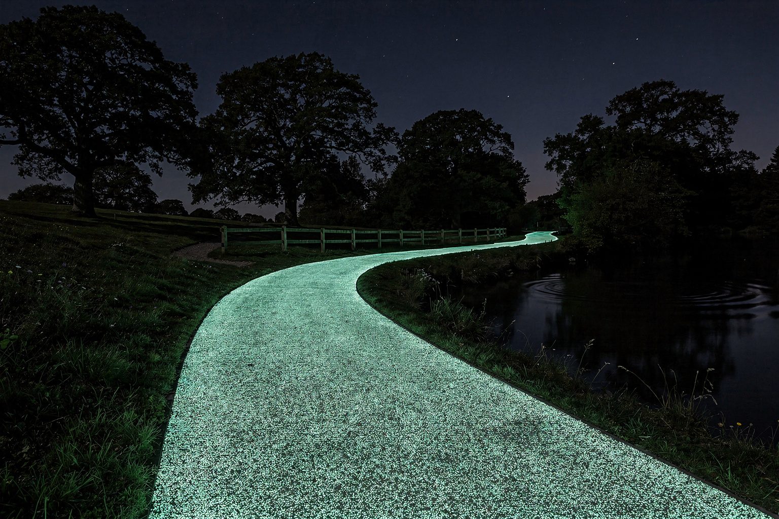 Illustration: a footpath paved with glow-in-the-dark aggregate shining aqua-green through a dark park at night